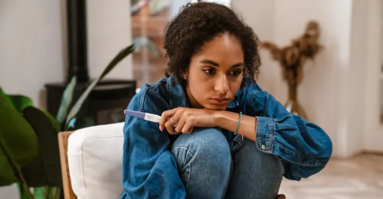 A young woman sitting with a pregnancy test in hand, looking sad representing the emotional impact of a chemical pregnancy.